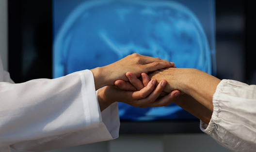 arts onderzoekt de hand van een patien met op de achtergrond een brain scan